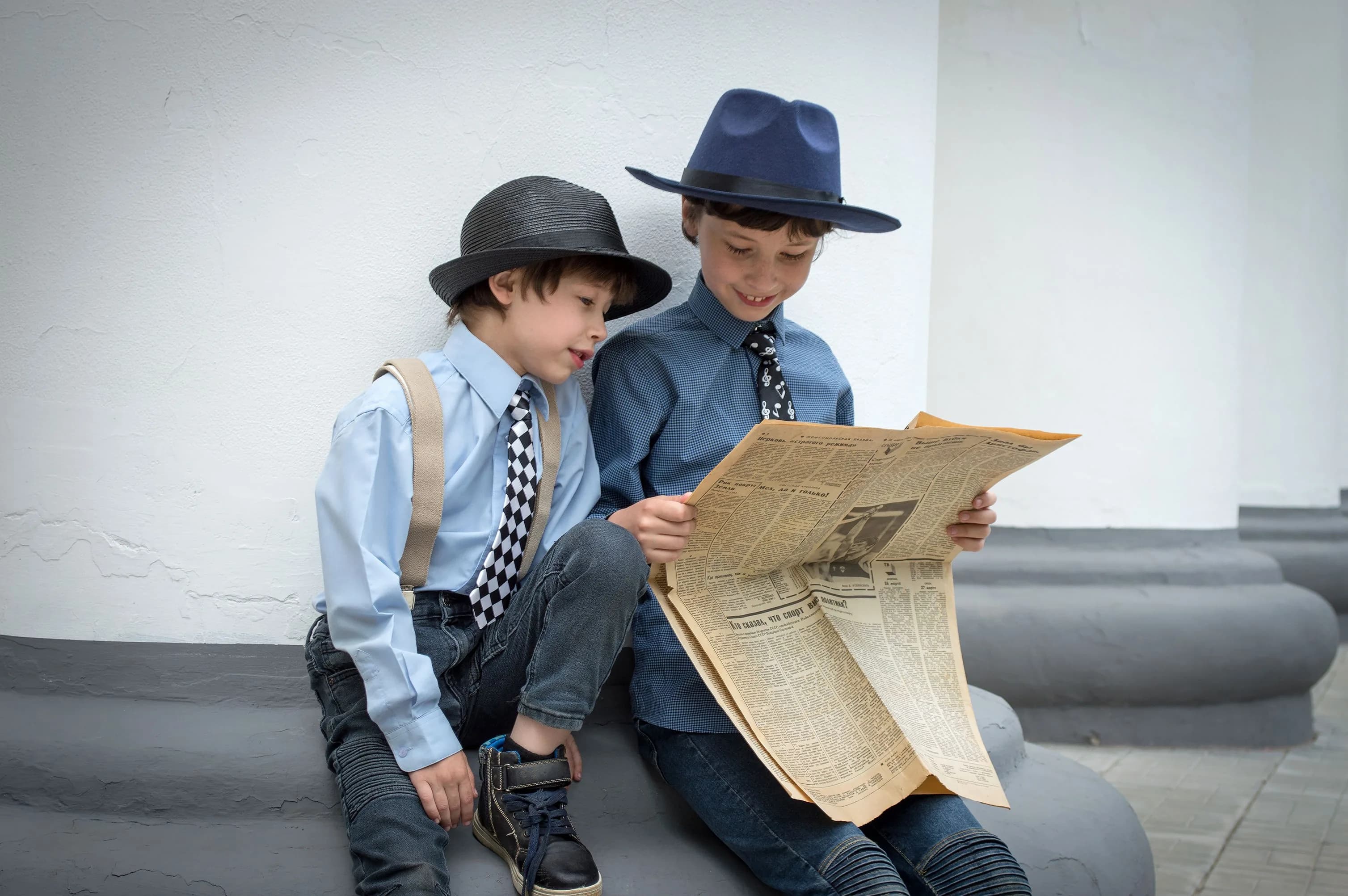 Two smartly dressed boys sitting outside reading a newspaper together